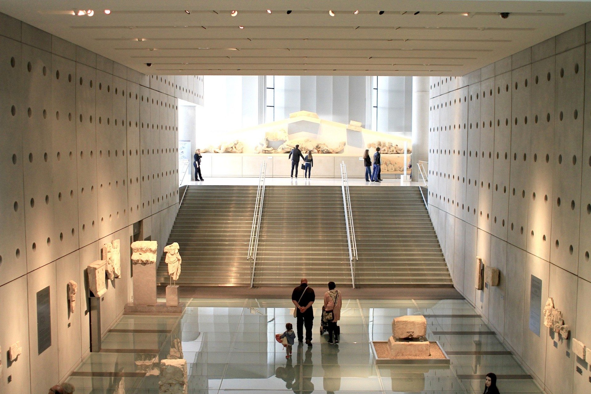 Aufsteigend. Eine gläserne Rampe und marmorne Freitreppe führt in den oberen Ausstellungssaal. Der Rundgang soll an den beschwerlichen Aufstieg auf den Tempelberg erinnern. Dieses Gefühl wird durch den Wechsel der Raumhöhe von fünf Metern auf das Dreifache verstärkt.