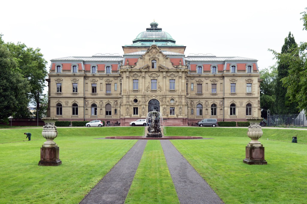 Der Gerichtssitz nutzt das historische Residenz-Palais (Architekt: Josef Durm, 1897) seit 1950 – Umnutzung statt Neubau. Die Schale bleibt lesbar, die Funktion ist Gegenwart: Rechtsstaat im gewachsenen Stadtgefüge.
