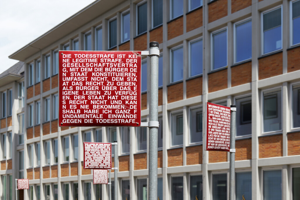 24 doppelseitige Schilder versammeln Stimmen von Richter:innen, Jurist:innen und Bürger:innen; zentral zwischen Zirkel und Schloss sowie dezentral im Stadtgebiet. Das 2005 eingeweihte Kunstwerk macht Recht und Unrecht als offene Debatte erfahrbar – kein Denkmal, sondern eine Fragestellung im Stadtraum. Es ist Karlsruhes prägnantestes Bild für sichtbare Grundrechte. 