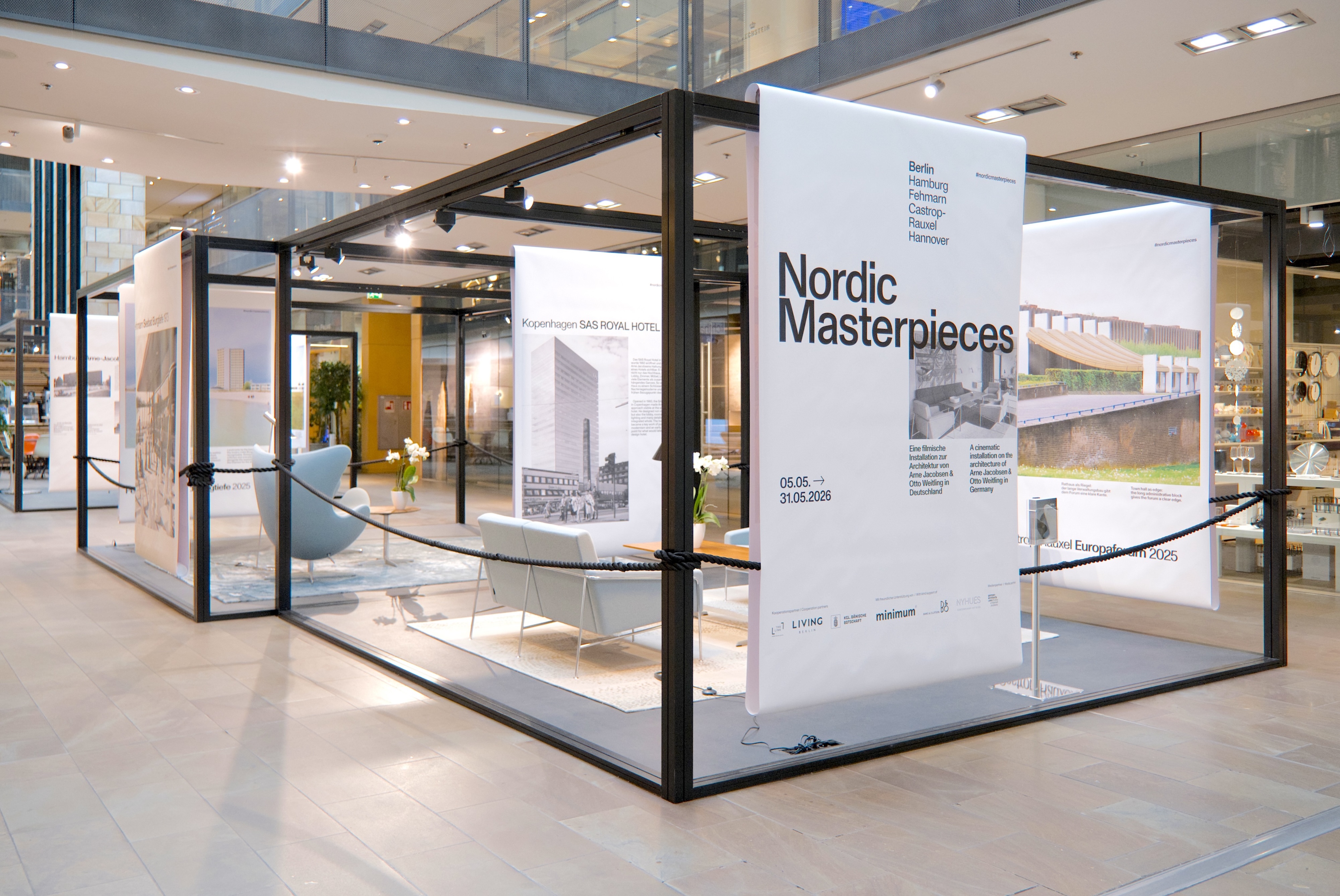 Aus der Schräge wird die räumliche Ordnung der Installation sichtbar: offene Kuben, dazwischen Wege, Sichtachsen und frei hängende Banner.