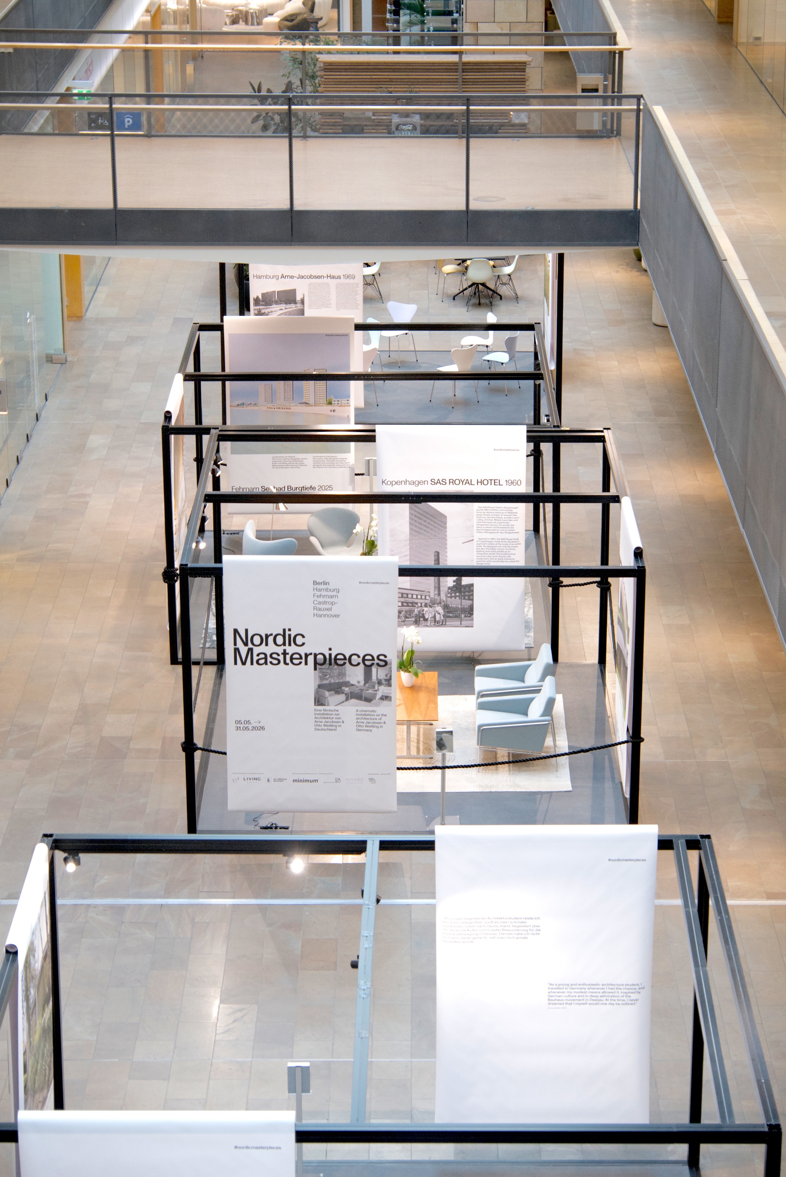 Die Aufnahme aus der Höhe zeigt die Berliner Installation als Folge offener Kuben im Foyer im Atrium des LIVING BERLIN. Banner und Sitzbereiche gliedern die fünf Stationen, ohne den Raum vollständig abzuschließen.