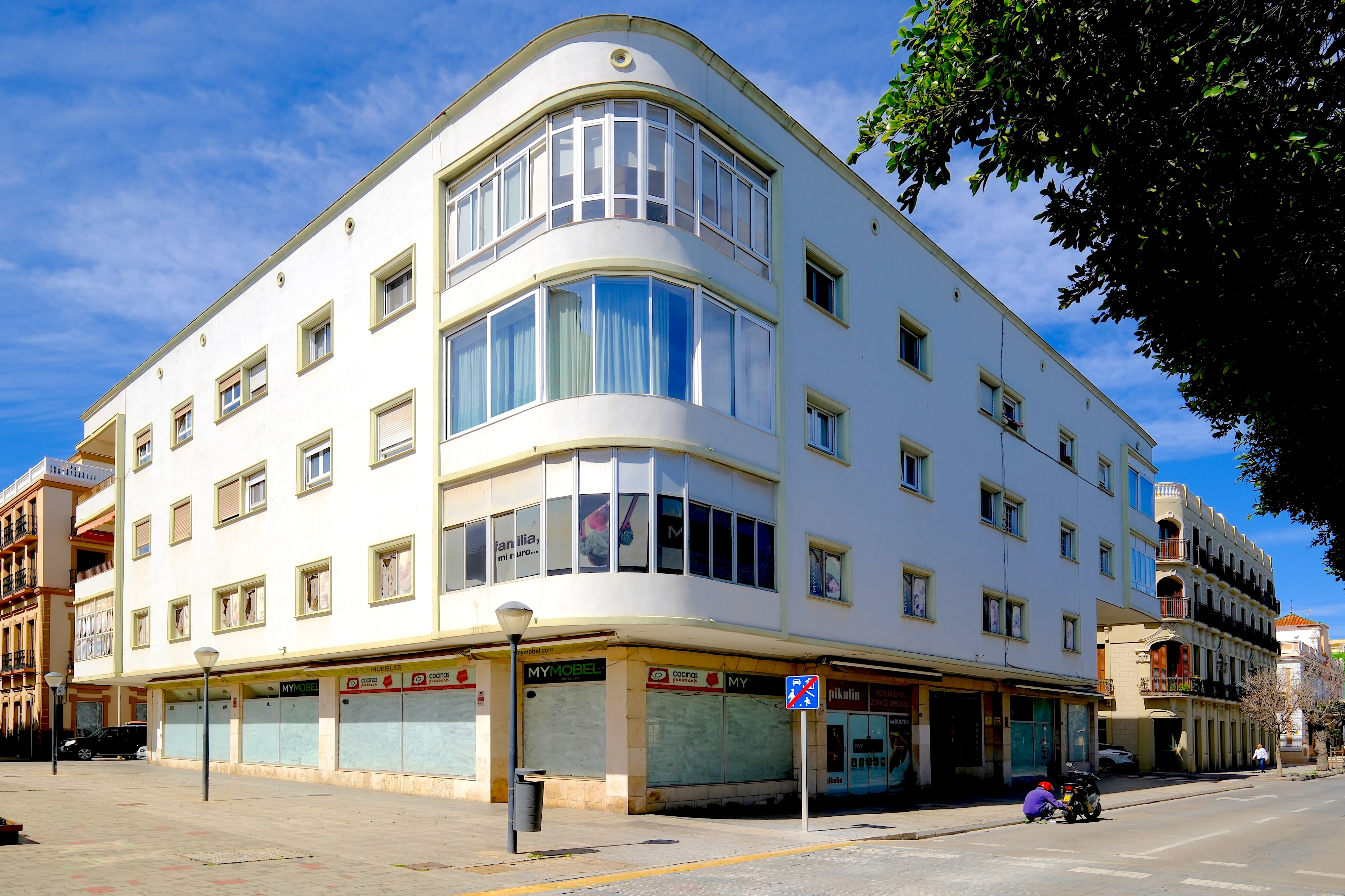 Das Wohn- und Geschäftshaus mit der hellen, schlichten Fassade und der gerundeten, verglasten Ecke hebt sich deutlich vom nahen Modernisme-Viertel ab und zeugt von einer anderen Formensprache ab den 1940er- und 1950er-Jahren.